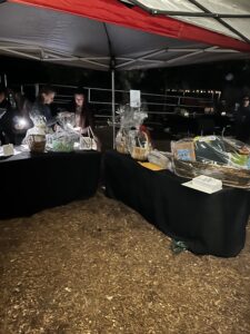 Tables covered with black tablecloth and several baskets lined up at night under an EZ-Up awning.